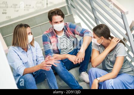 Couple of students wearing masks relaxing in the campus Stock Photo