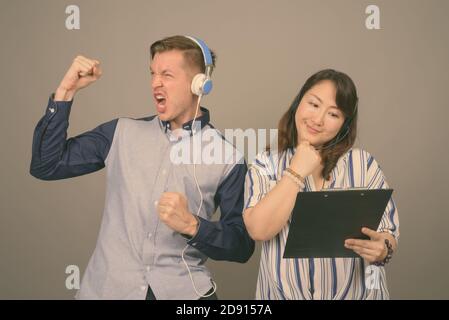 Young handsome businessman and mature Asian businesswoman against gray background Stock Photo