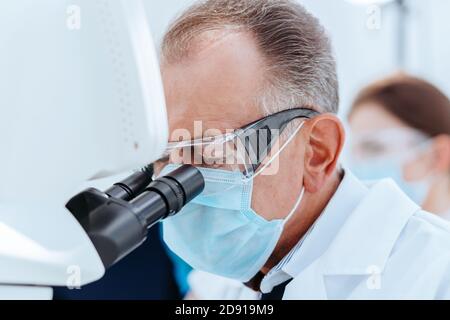 scientist in a protective mask looking through a microscope. Stock Photo