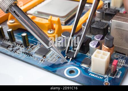 A MOSFET transistor key is soldered out of the computer Board using a soldering iron and tweezers Stock Photo