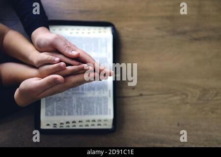 Religious Christian girl praying with her mother indoors. Bible in background. Space for text Stock Photo