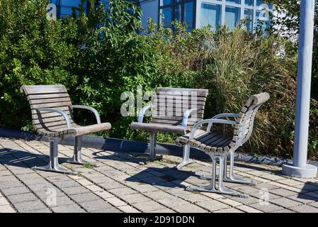 Three outdoor park armchairs made of metal and weathered wood sit are grouped facing each other, to enable conversation. Stock Photo