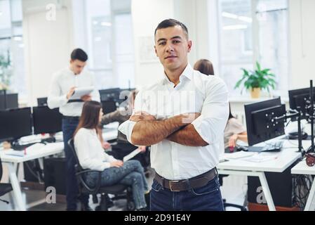Man in formal wear standing in the office against young people that works together in the office Stock Photo