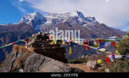 Multi-colored Buddhist prayer flags attached to a pile of stones flying in the wind above village Namche Bazar, Khumbu, Himalayas, Nepal. Stock Photo