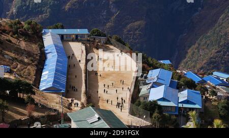 Aerial view of school with blue colored corrugated iron roof located in Namche Bazar, Khumbu, Himalayas, Nepal with children playing on the schoolyard. Stock Photo