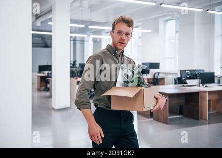 Office worker in formal wear walking with box with green plant inside of it Stock Photo