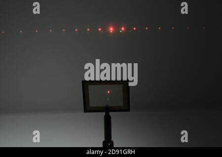 In a darkened room, two laser beams from a source under the camera, hits an optical grid and an interference pattern apppears on the wall in the backg Stock Photo