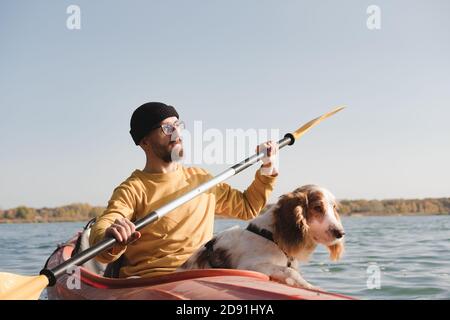 Kayaking with dogs: man rowing a boat on the lake with his spaniel. Active rest and adventures with pets, riding a canoe with dog Stock Photo