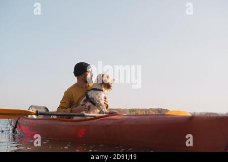 Kayaking with dogs: man sits in a row boat on the lake next to his spaniel. Active rest and adventures with pets, riding a canoe with dog Stock Photo