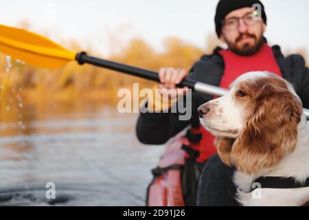 Man rowing a canoe with his spaniel dog, sunny autumn weather. Going kayak boating with dogs on the river, active pets, happy dog and owner on an adve Stock Photo