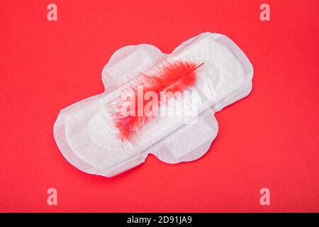 Red feather on a sanitary pad on a red background Stock Photo