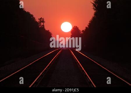 A double set of railroad tracks lead to infinity and a firey sunset Stock Photo