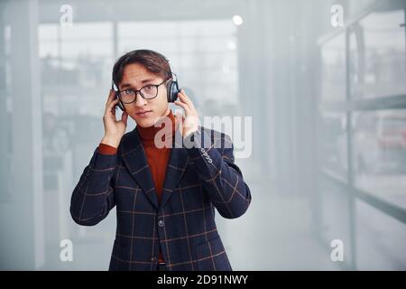 Listening to the music in headphones. Young business man in luxury suit and formal clothes is indoors in the office Stock Photo