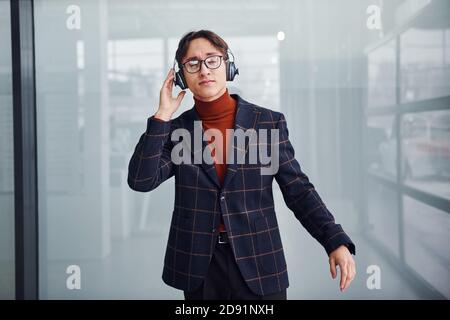 Listening to the music in headphones. Young business man in luxury suit and formal clothes is indoors in the office Stock Photo