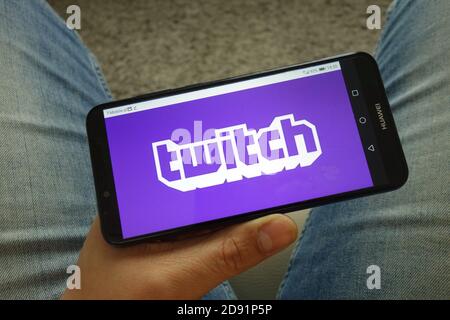 Man holding smartphone with Twitch video live streaming service logo Stock Photo