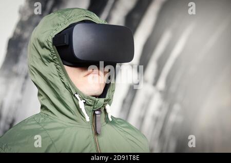 serious young man with a virtual reality headset in a green protective jacket, remote monitoring and military operation using virtual technology Stock Photo