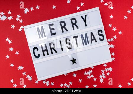 Merry Christmas text displayed on a lightbox with white star shaped confetti Stock Photo