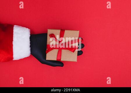 Hand in protective glove holds a red gift box with a ribbon Stock Photo