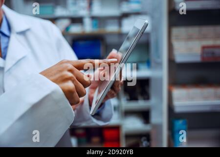 Close up of senior pharmacist scrolling on digital tablet looking for prescription medications standing in chemist  Stock Photo