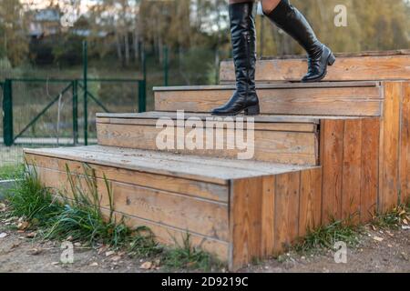 A joyful woman walks up the stairs in burgundy pall and biret, with a beautiful smile in black clothes, in the fall against the background of a pond Stock Photo