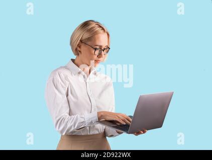 Portrait of focused businesswoman using laptop computer over blue studio background Stock Photo