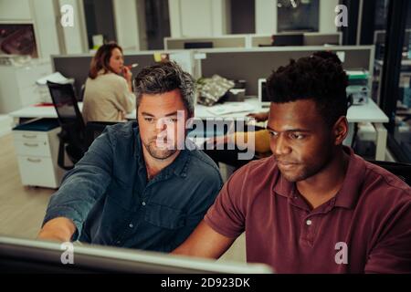 Caucasian and African American business men working on collaboration project together on desktop computer  Stock Photo