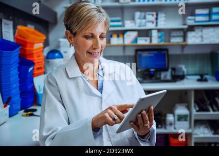 Caucasian female pharmacist scrolling through emails on digital tablet standing in pharmacy  Stock Photo