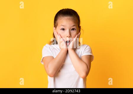Asian kid with open mouth touching cheeks in excitement Stock Photo