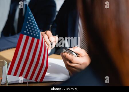 partial view of journalist with dictaphone holding pen while interviewing politicians during press conference, blurred foreground Stock Photo