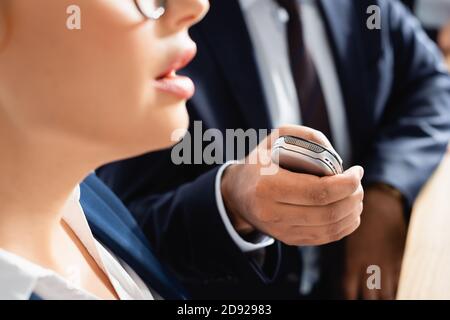partial view of journalist with dictaphone interviewing politician during press conference, blurred foreground Stock Photo