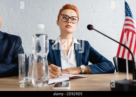 Focused woman writing in notebook, while sitting near colleague in boardroom during political party meeting Stock Photo