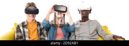 Panoramic shot of smiling multiethnic teenagers using vr headsets on couch isolated on white Stock Photo