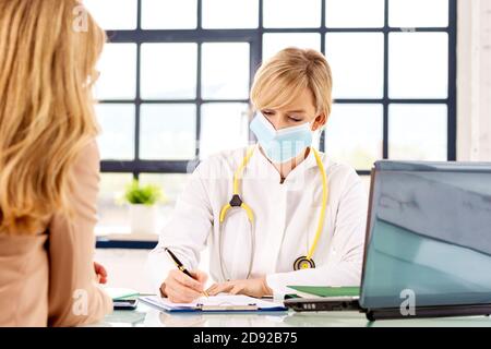 Shot of attractive female doctor talking to her patient while sitting at office desk in doctor’s room. Stock Photo