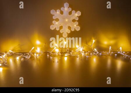 Garland of shining light bulbs and big snowflake on golden background for Christmas mockup. Glowing snowflake toy and Christmas lights on golden Stock Photo