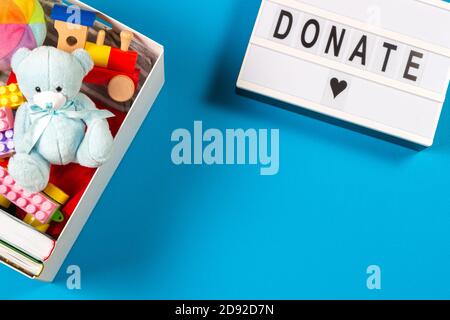 Donation concept. White lightbox with text donate and donation box with toys books clothing and on light blue background. Top view Stock Photo