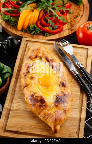 Ajarian Khachapuri traditional Georgian cheese pastry with eggs on cutting board. Homemade baking. Stock Photo