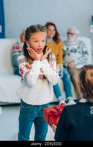 selective focus of excited girl holding hands near face while looking at brother holding christmas present Stock Photo