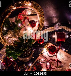 Christmas still life of a book, Christmas baubles, golden balls, ribbons and a plant reflecting in a golden mirror Stock Photo