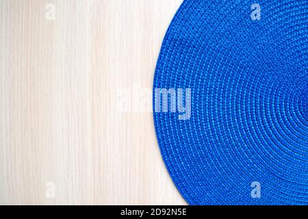 Blue round woven textile mat on beige wooden background. Copy space, top view Stock Photo