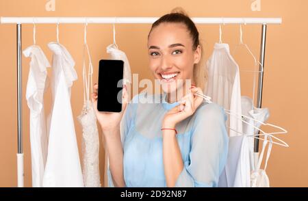 Smiling lady showing black phone screen and hangers Stock Photo