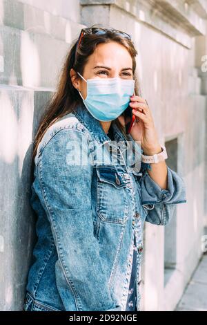 happy woman with a face mask talks on the phone while walking down the street Stock Photo