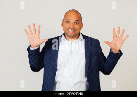Portrait of successful young African American businessman guy, showing with fingers to number ten, smiling, confident and happy. The man shows ten fingers. Number 10. Standing on a gray background Stock Photo