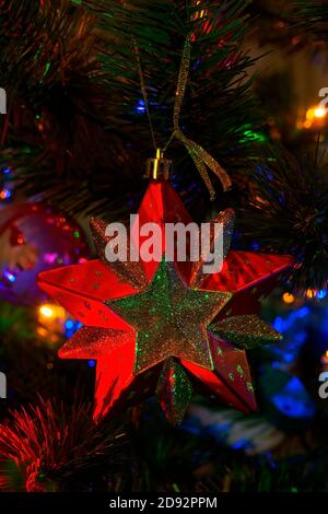 Red toy in the form of a star hangs on a christmas tree with garlands Stock Photo