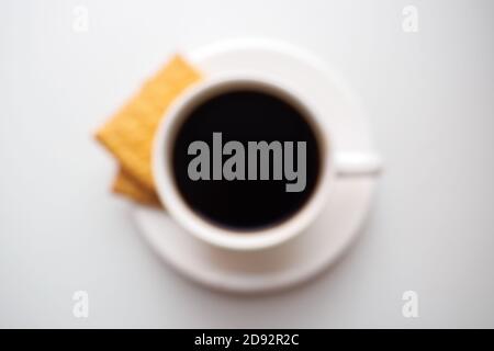blurred cup of coffee with crackers on saucer on white background, top view Stock Photo
