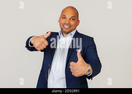 Portrait of a successful young African American guy businessman making a positive hand gesture approvingly, smiling thumbs up and happy for success. Winner's gesture. Standing on a gray background Stock Photo