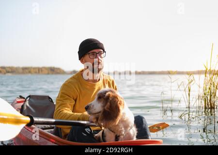 Man with a dog in a canoe on the lake. Young male person with spaniel in a kayak row boat, active free time with pets, companionship, adventure dogs Stock Photo
