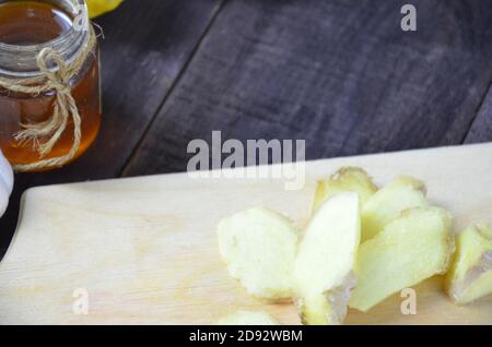 Ginger on cutting board, jar of honey, dried lemon slice, cinnamon and grater on kitchen table. Selective focus. Stock Photo