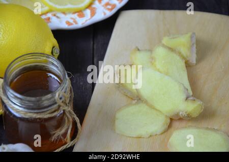 Ginger on cutting board, jar of honey, dried lemon slice, cinnamon and grater on kitchen table. Selective focus. Stock Photo