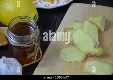 Ginger on cutting board, jar of honey, dried lemon slice, cinnamon and grater on kitchen table. Selective focus. Stock Photo