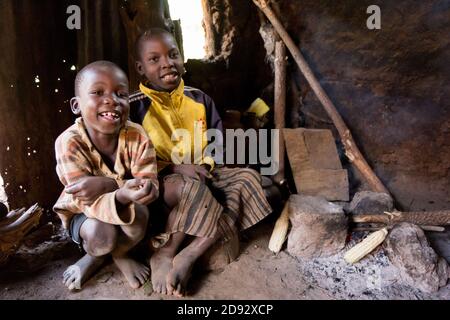 Two boys sitting at a fire/embers in a wattle-and-daub house in rural Uganda. Stock Photo